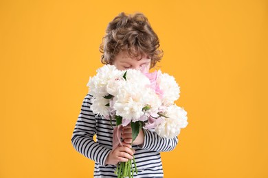 Photo of Cute little boy with bouquet of beautiful peonies on yellow background