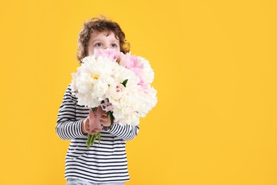 Photo of Cute little boy with bouquet of beautiful peonies on yellow background. Space for text