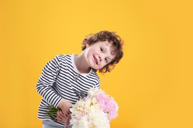 Photo of Cute little boy with bouquet of beautiful peonies on yellow background