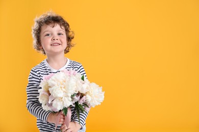 Photo of Cute little boy with bouquet of beautiful peonies on yellow background. Space for text