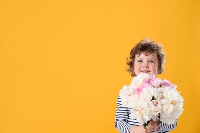 Photo of Cute little boy with bouquet of beautiful peonies on yellow background. Space for text