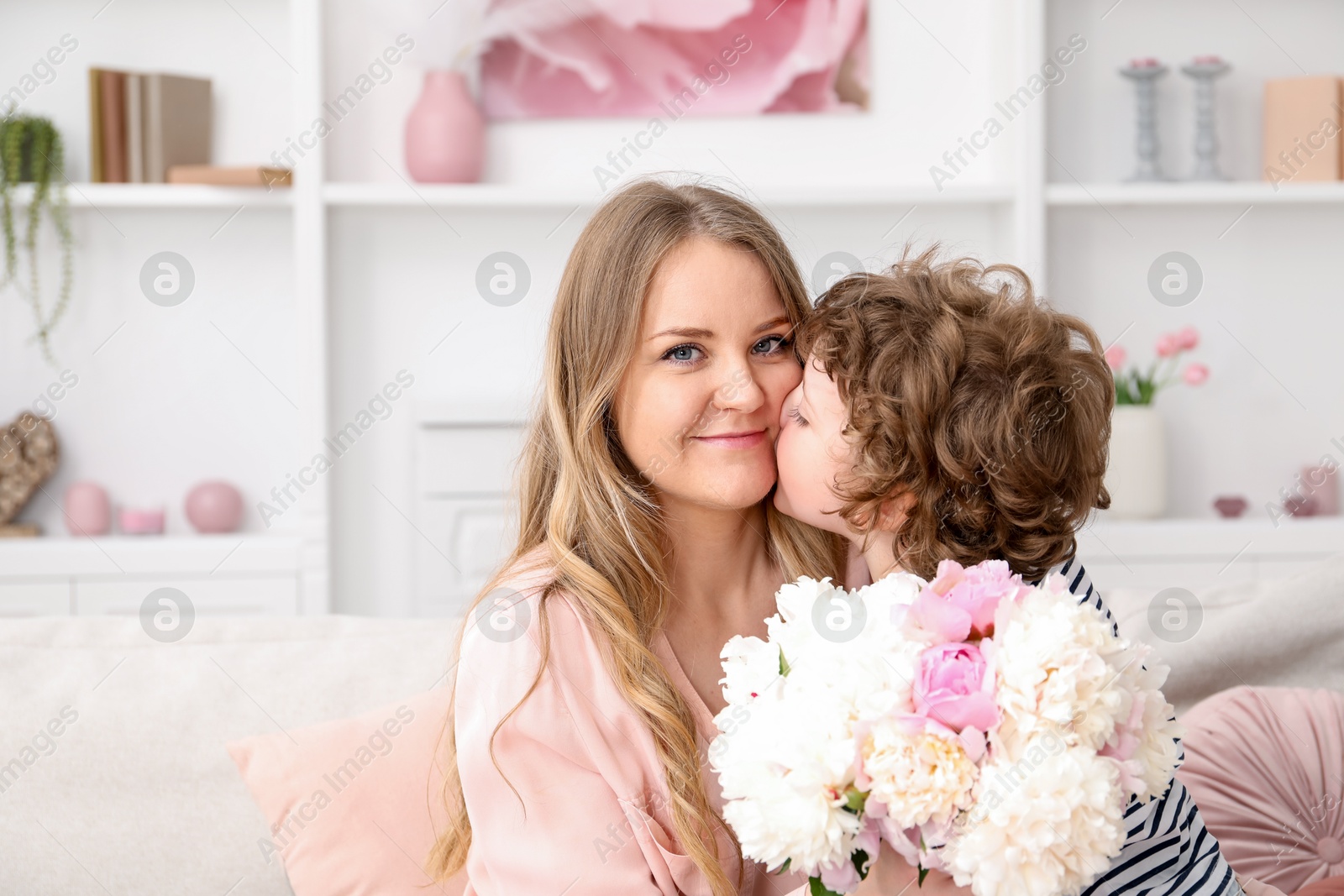 Little boy kissing his mom and giving her beautiful peony flowers at home. Space for text Photo of Little boy kissing his mom and giving her beautiful peony flowers at home. Space for text