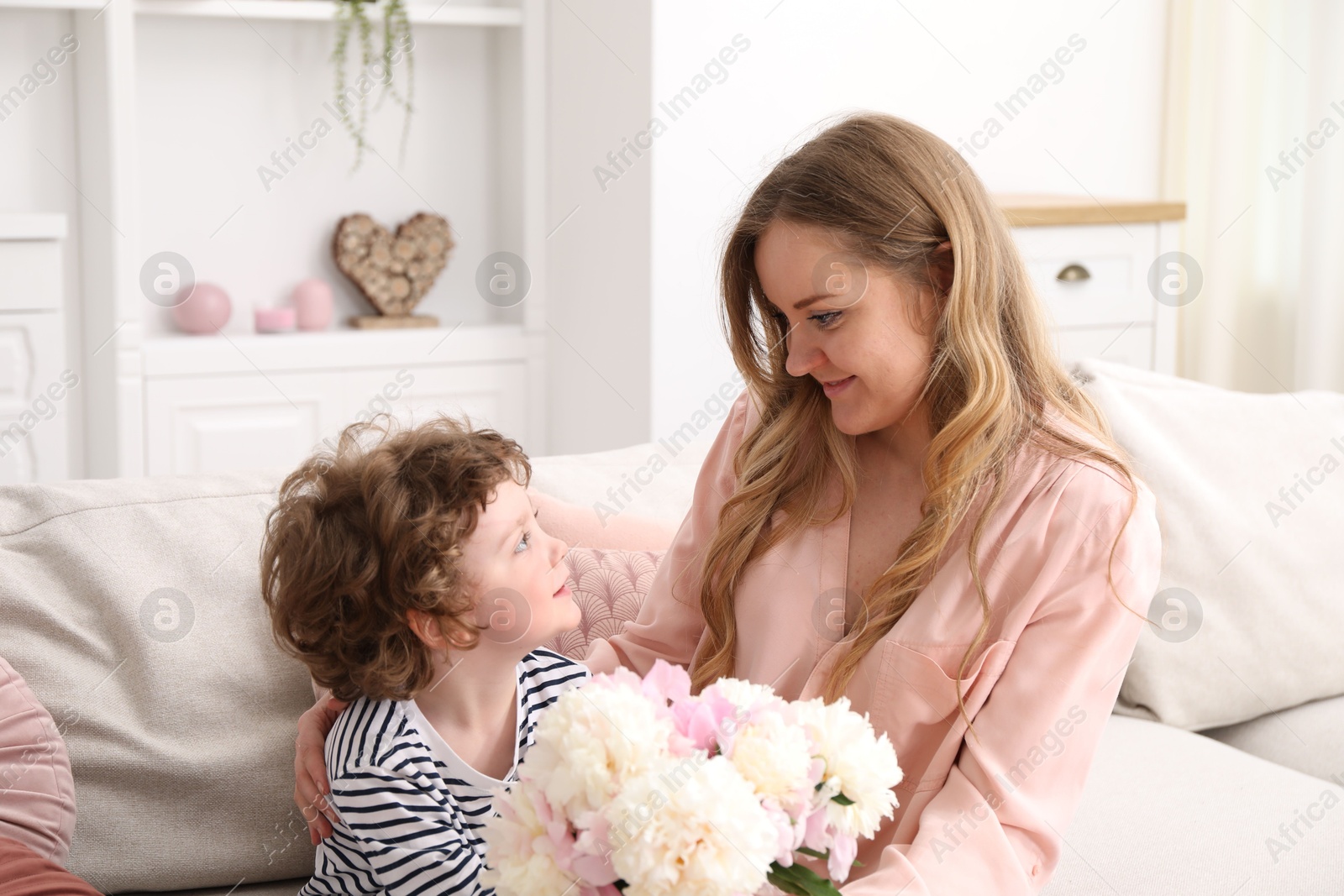 Little boy giving his mom beautiful peony flowers on sofa at home Photo of Little boy giving his mom beautiful peony flowers on sofa at home
