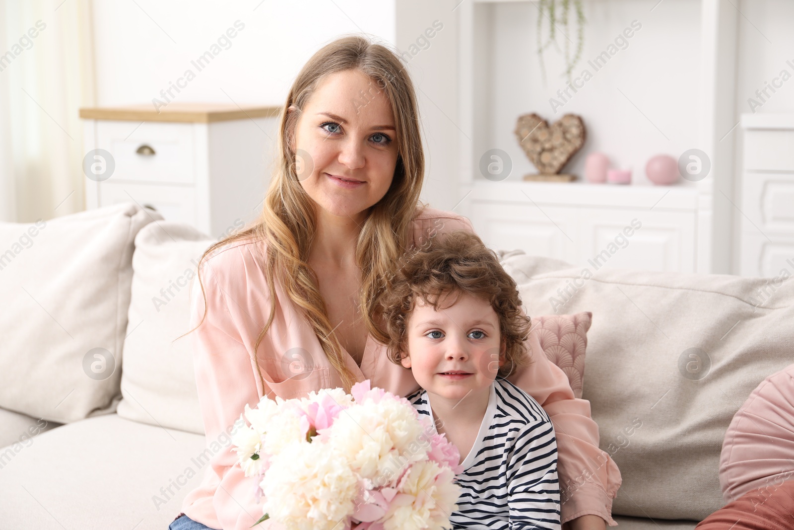 Little boy giving his mom beautiful peony flowers on sofa at home Photo of Little boy giving his mom beautiful peony flowers on sofa at home