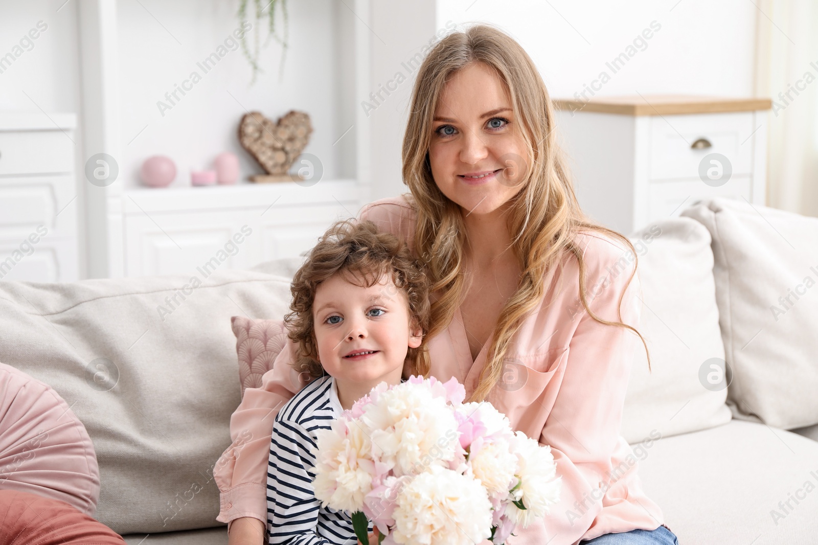 Little boy giving his mom beautiful peony flowers on sofa at home Photo of Little boy giving his mom beautiful peony flowers on sofa at home