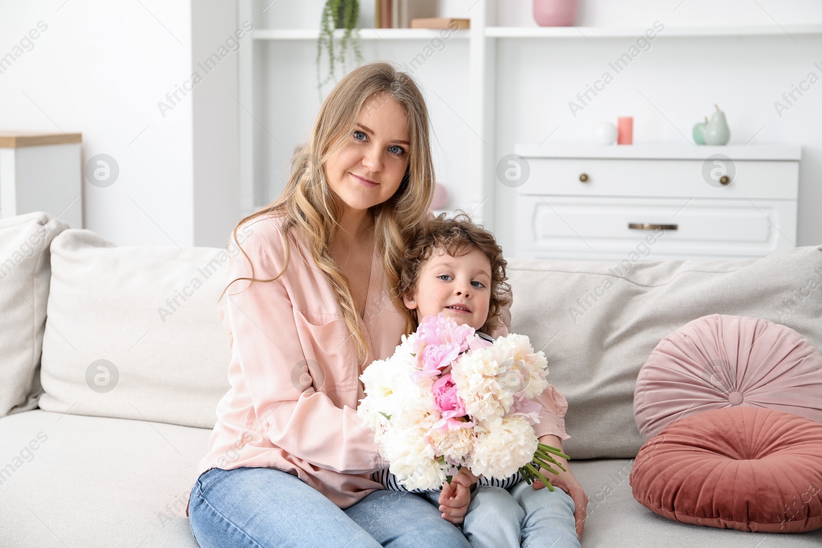 Little boy giving his mom beautiful peony flowers on sofa at home Photo of Little boy giving his mom beautiful peony flowers on sofa at home