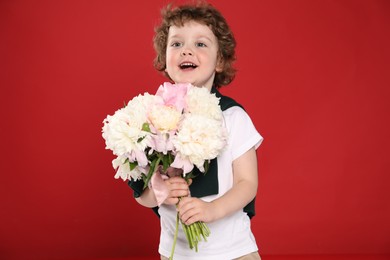 Photo of Cute little boy with bouquet of beautiful peonies on red background
