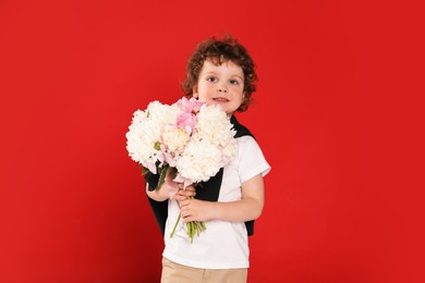 Photo of Cute little boy with bouquet of beautiful peonies on red background