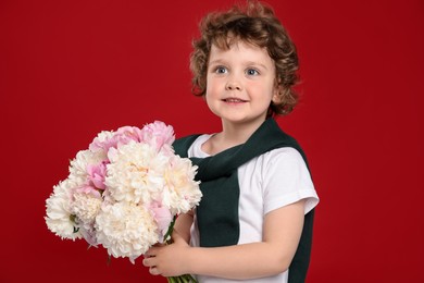 Photo of Cute little boy with bouquet of beautiful peonies on red background