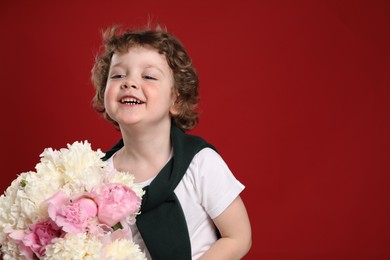 Photo of Cute little boy with bouquet of beautiful peonies on red background. Space for text