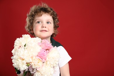 Photo of Cute little boy with bouquet of beautiful peonies on red background. Space for text