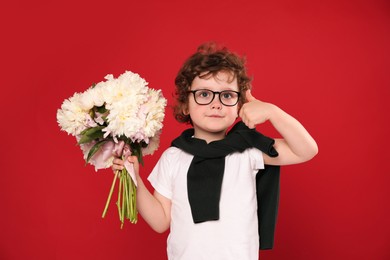 Photo of Cute little boy with bouquet of beautiful peonies showing thumbs up on red background