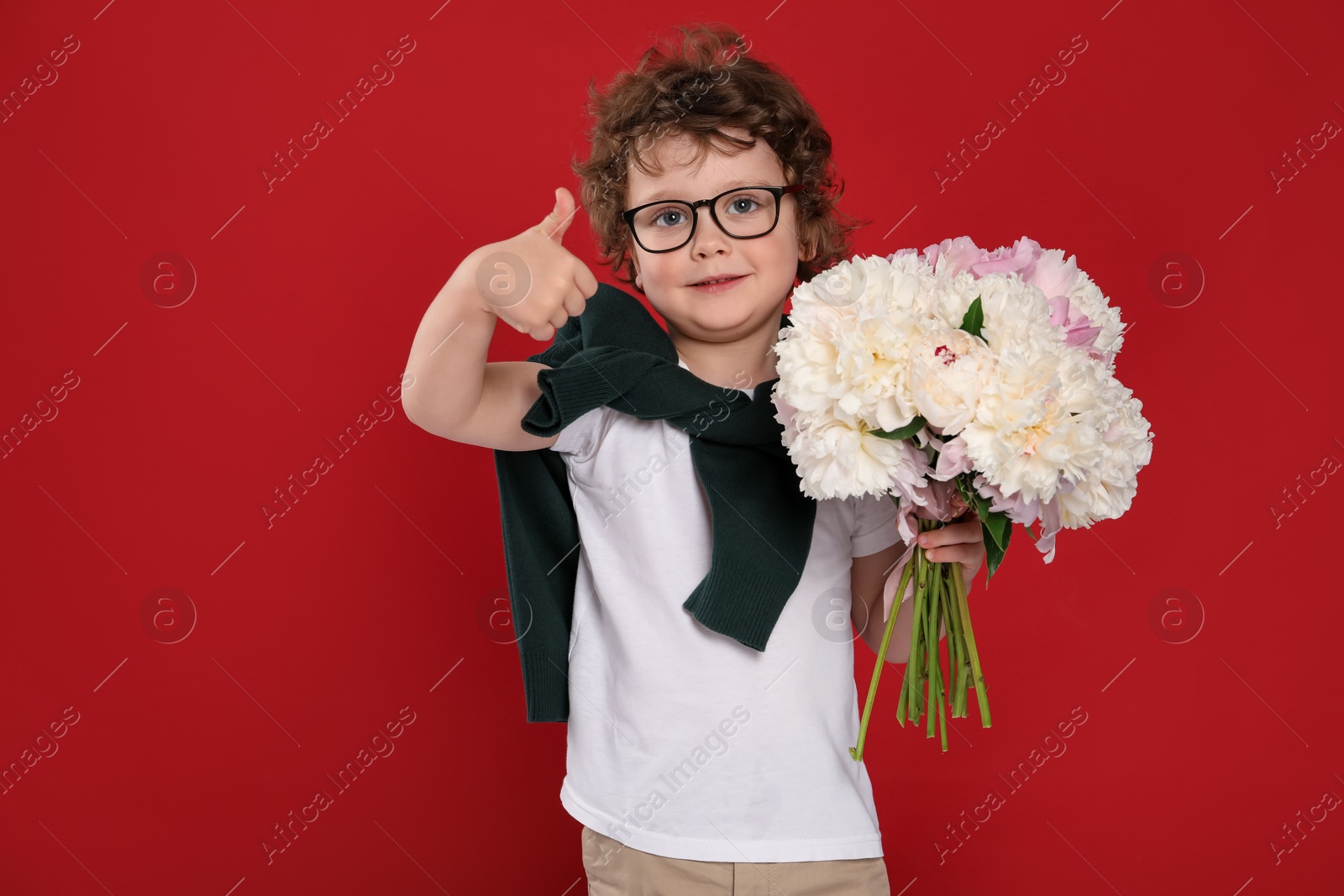 Cute little boy with bouquet of beautiful peonies showing thumbs up on red background Photo of Cute little boy with bouquet of beautiful peonies showing thumbs up on red background