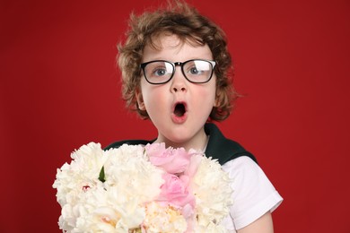 Photo of Cute little boy with bouquet of beautiful peonies on red background