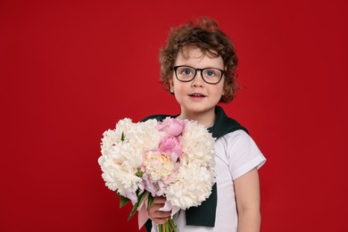 Photo of Cute little boy with bouquet of beautiful peonies on red background