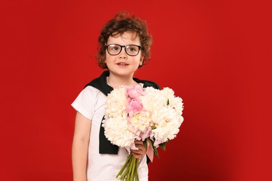 Photo of Cute little boy with bouquet of beautiful peonies on red background