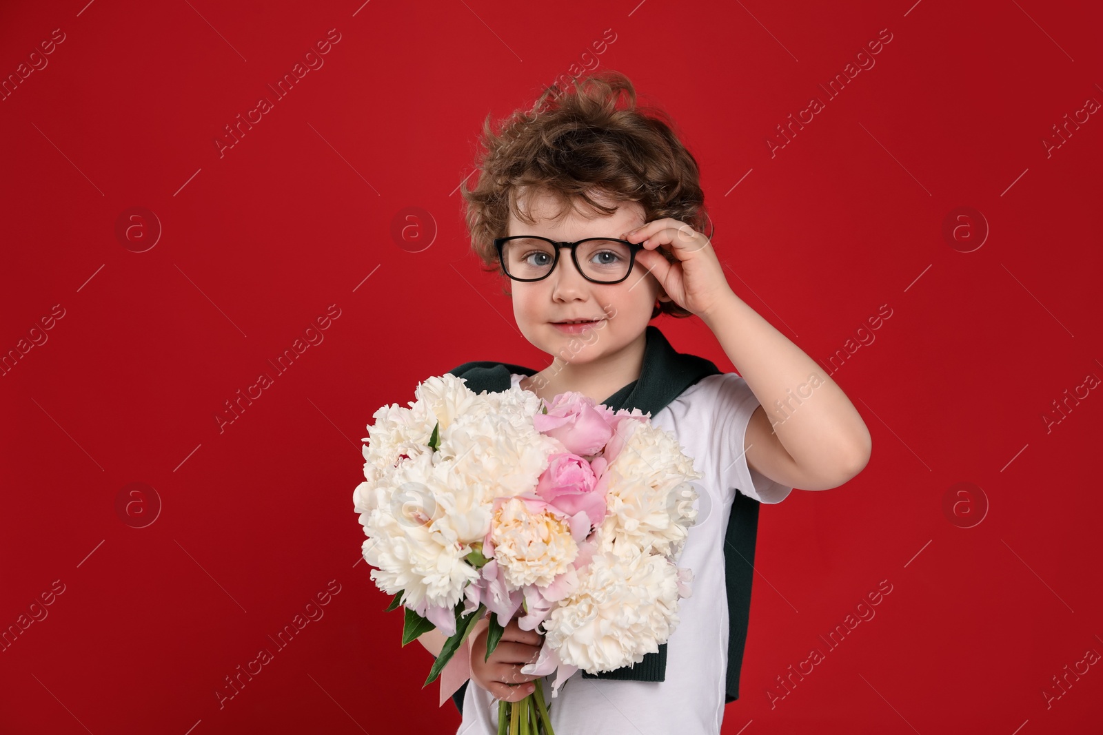 Cute little boy with bouquet of beautiful peonies on red background Photo of Cute little boy with bouquet of beautiful peonies on red background