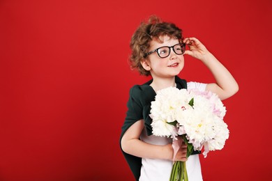 Photo of Cute little boy with bouquet of beautiful peonies on red background. Space for text