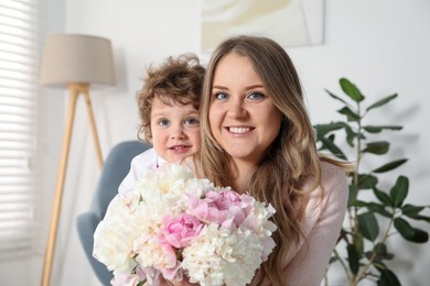Photo of Little boy giving his mom beautiful peony flowers at home