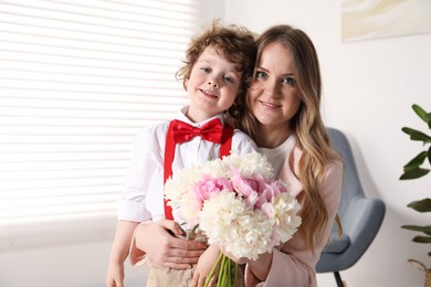 Photo of Little boy giving his mom beautiful peony flowers at home