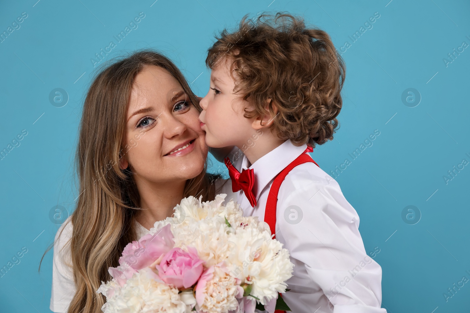 Little boy kissing his mom and giving her beautiful peony flowers on light blue background Photo of Little boy kissing his mom and giving her beautiful peony flowers on light blue background