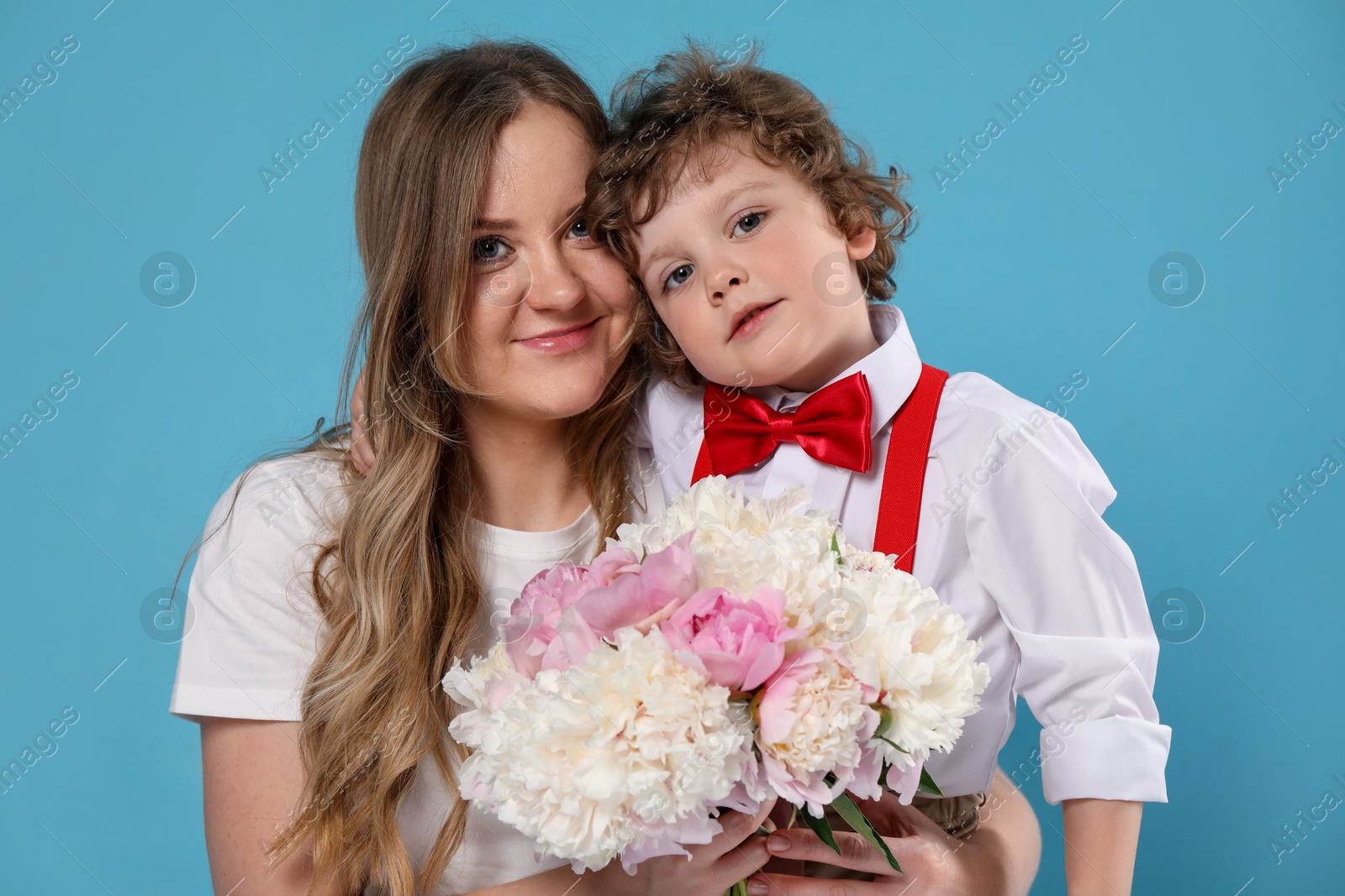 Little boy giving his mom beautiful peony flowers on light blue background Photo of Little boy giving his mom beautiful peony flowers on light blue background