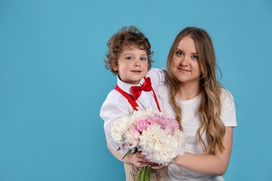 Photo of Little boy giving his mom beautiful peony flowers on light blue background