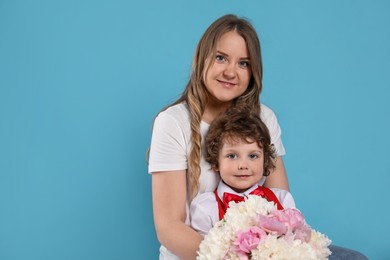 Photo of Little boy giving his mom beautiful peony flowers on light blue background. Space for text