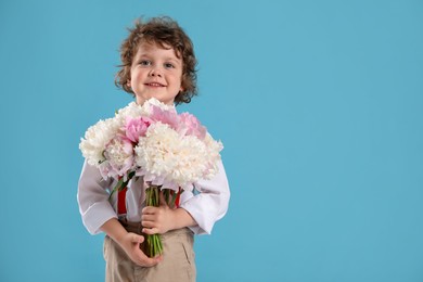 Photo of Cute little boy with bouquet of beautiful peonies on light blue background. Space for text