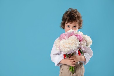 Photo of Cute little boy with bouquet of beautiful peonies on light blue background. Space for text