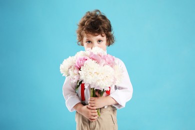 Photo of Cute little boy with bouquet of beautiful peonies on light blue background