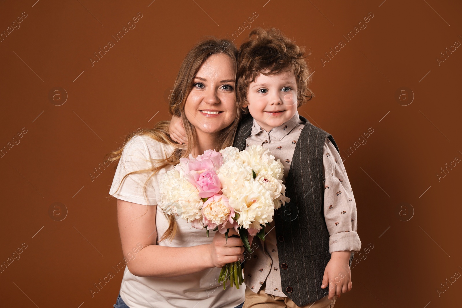 Little boy giving his mom beautiful peony flowers on brown background Photo of Little boy giving his mom beautiful peony flowers on brown background