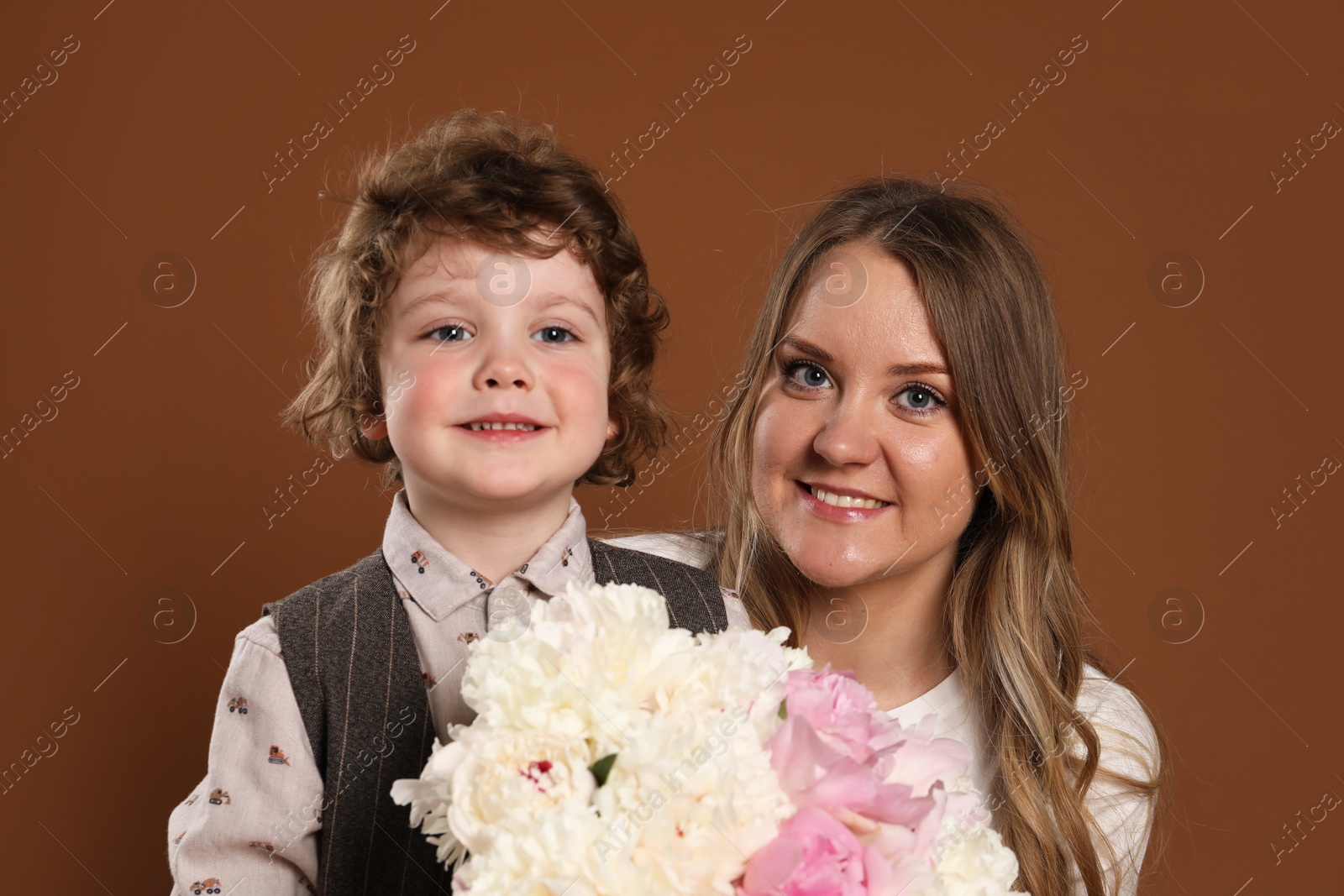 Little boy giving his mom beautiful peony flowers on brown background Photo of Little boy giving his mom beautiful peony flowers on brown background