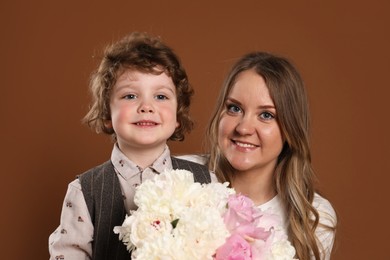 Photo of Little boy giving his mom beautiful peony flowers on brown background