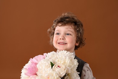 Photo of Cute little boy with bouquet of beautiful peonies on brown background