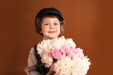 Photo of Cute little boy with bouquet of beautiful peonies on brown background