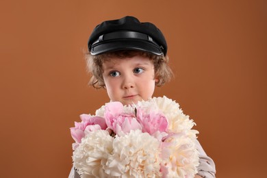 Photo of Cute little boy with bouquet of beautiful peonies on brown background