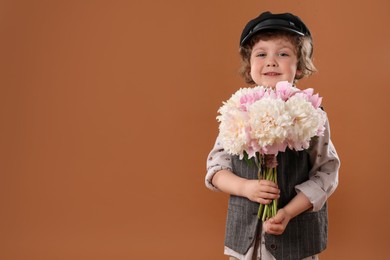 Photo of Cute little boy with bouquet of beautiful peonies on brown background. Space for text