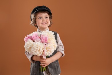 Photo of Cute little boy with bouquet of beautiful peonies on brown background. Space for text