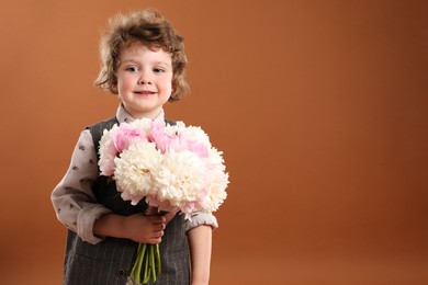 Photo of Cute little boy with bouquet of beautiful peonies on brown background. Space for text