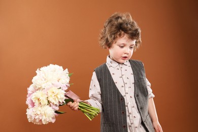 Photo of Cute little boy with bouquet of beautiful peonies on brown background