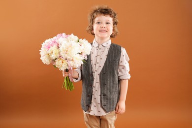 Photo of Cute little boy with bouquet of beautiful peonies on brown background