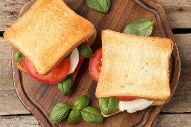 Photo of Tasty sandwiches with mozzarella cheese, tomatoes and basil on wooden table, top view
