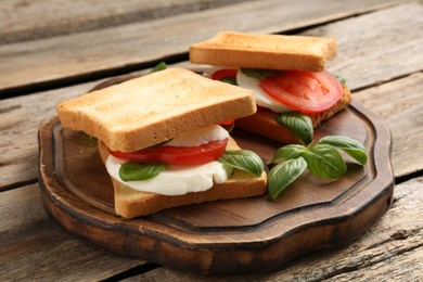 Photo of Tasty sandwiches with mozzarella cheese, tomatoes and basil on wooden table, closeup