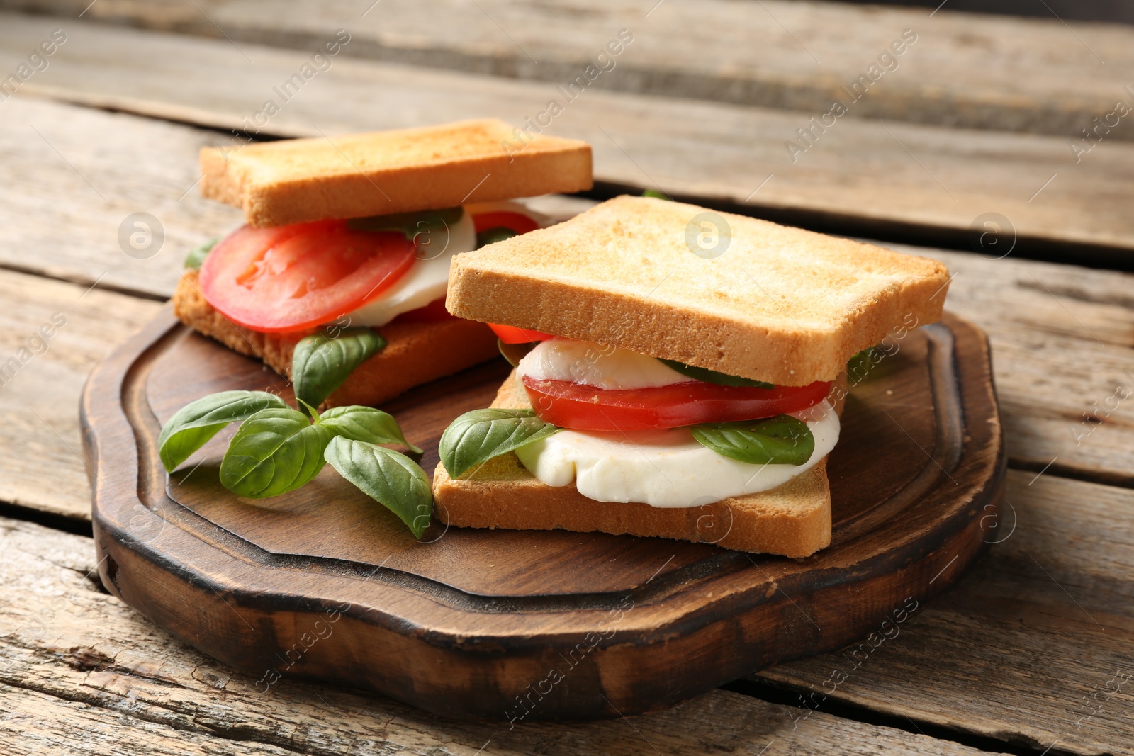 Tasty sandwiches with mozzarella cheese, tomatoes and basil on wooden table, closeup Photo of Tasty sandwiches with mozzarella cheese, tomatoes and basil on wooden table, closeup
