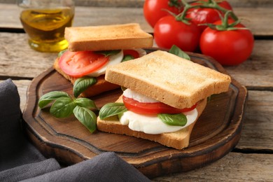 Photo of Tasty sandwiches with mozzarella cheese, tomatoes and basil on wooden table, closeup
