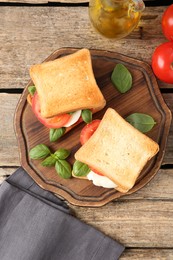 Photo of Tasty sandwiches with mozzarella cheese, tomatoes and basil on wooden table, flat lay