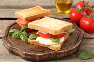 Photo of Tasty sandwiches with mozzarella cheese, tomatoes and basil on wooden table, closeup