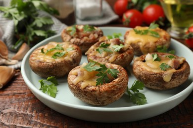 Photo of Tasty stuffed mushrooms and ingredients on wooden table, closeup