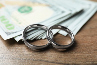 Photo of Silver wedding rings and dollar banknotes on wooden table, closeup